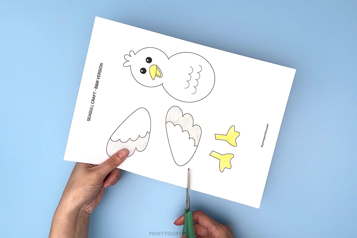 Cutting out a printable seagull craft template with scissors on a blue background
