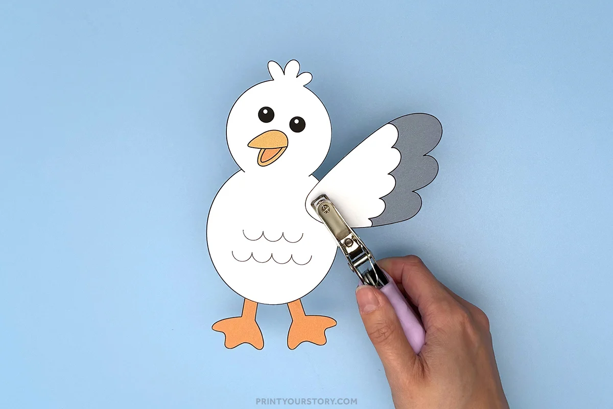 Hand using a hole punch on the wing of a paper seagull flapping craft