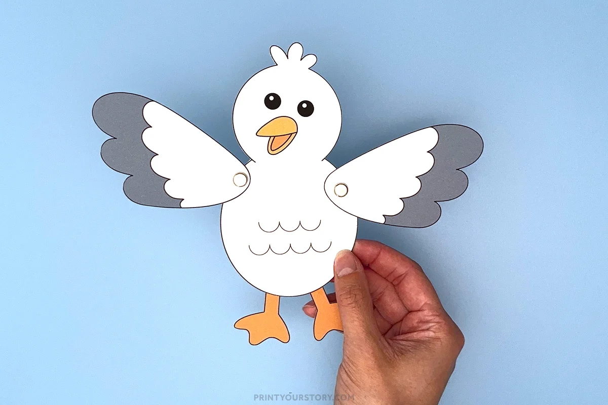 Hand holding a paper seagull craft with movable wings on a blue background