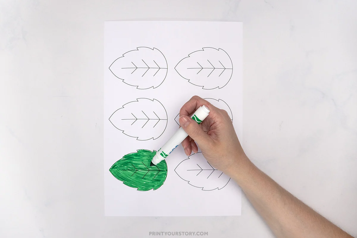 Hand coloring a leaf template green on a printable sheet for a kids hedgehog paper plate craft
