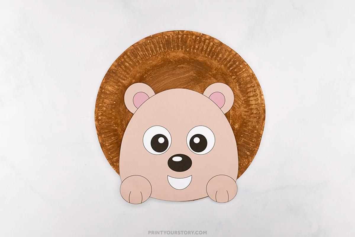 Finished paper plate hedgehog craft with brown painted plate, paper face, ears, paws, and large eyes