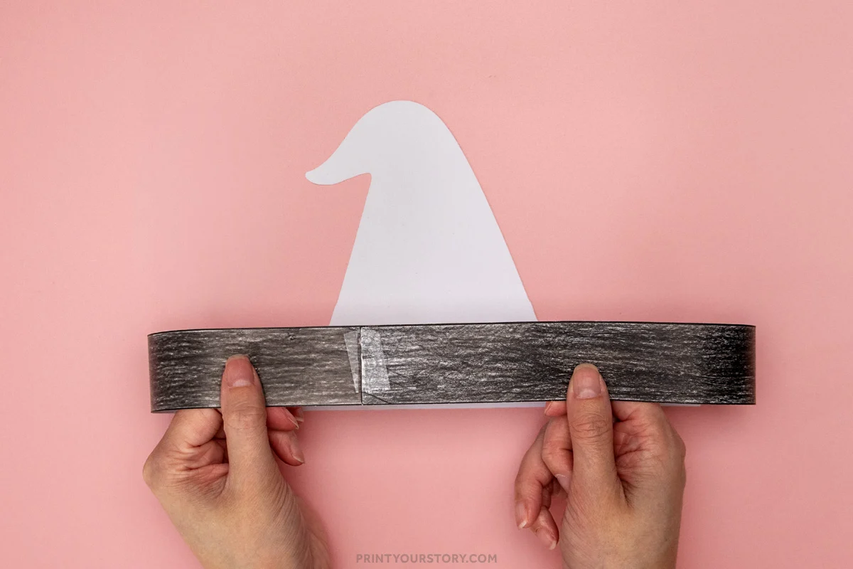 Hands holding a witch hat headband craft with a white hat cutout taped behind a black paper band