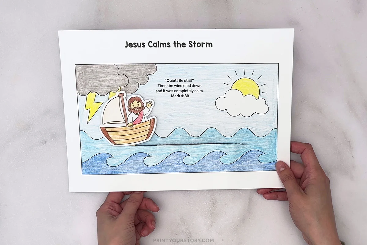 Hands holding a colored Jesus Calms the Storm printable with Jesus in a boat, waves, storm cloud, lightning, and sun
