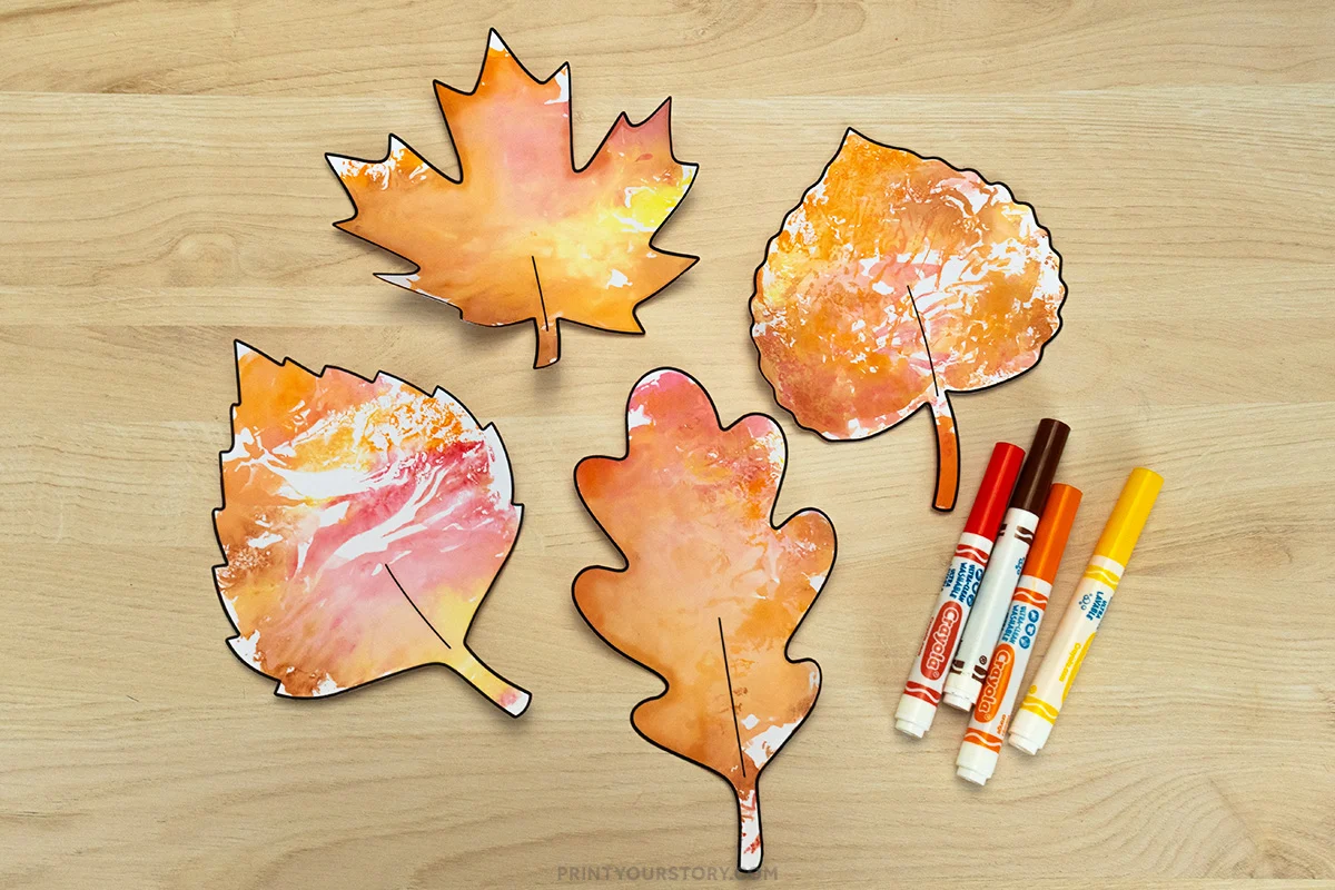 Painted fall leaf outline templates on a wooden table with four markers for a kids craft