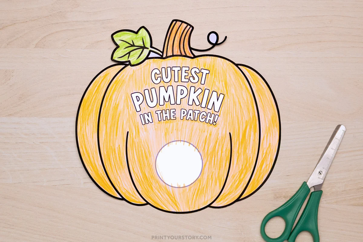 Colored pumpkin photo craft template with a circular cutout and scissors on a wooden surface