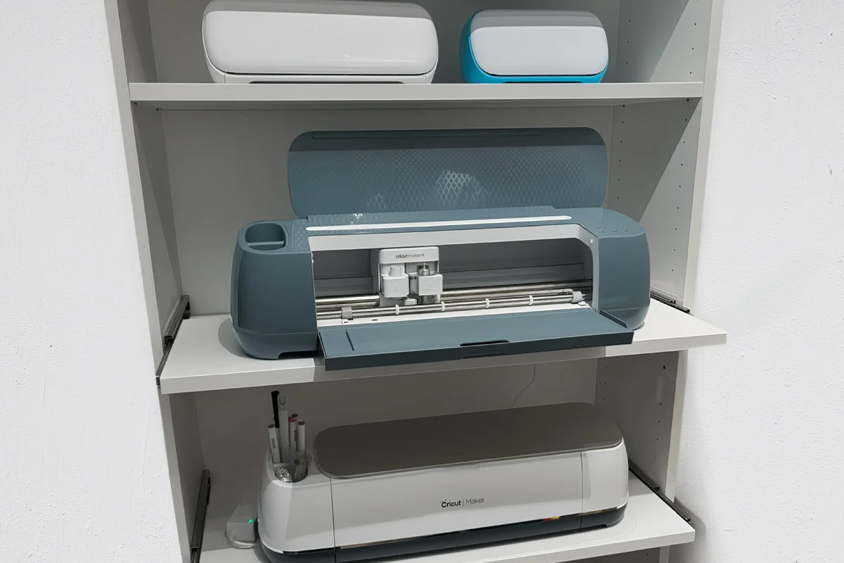 Three Cricut machines on shelves, including an open blue Cricut Maker 4 and a white Cricut Maker below