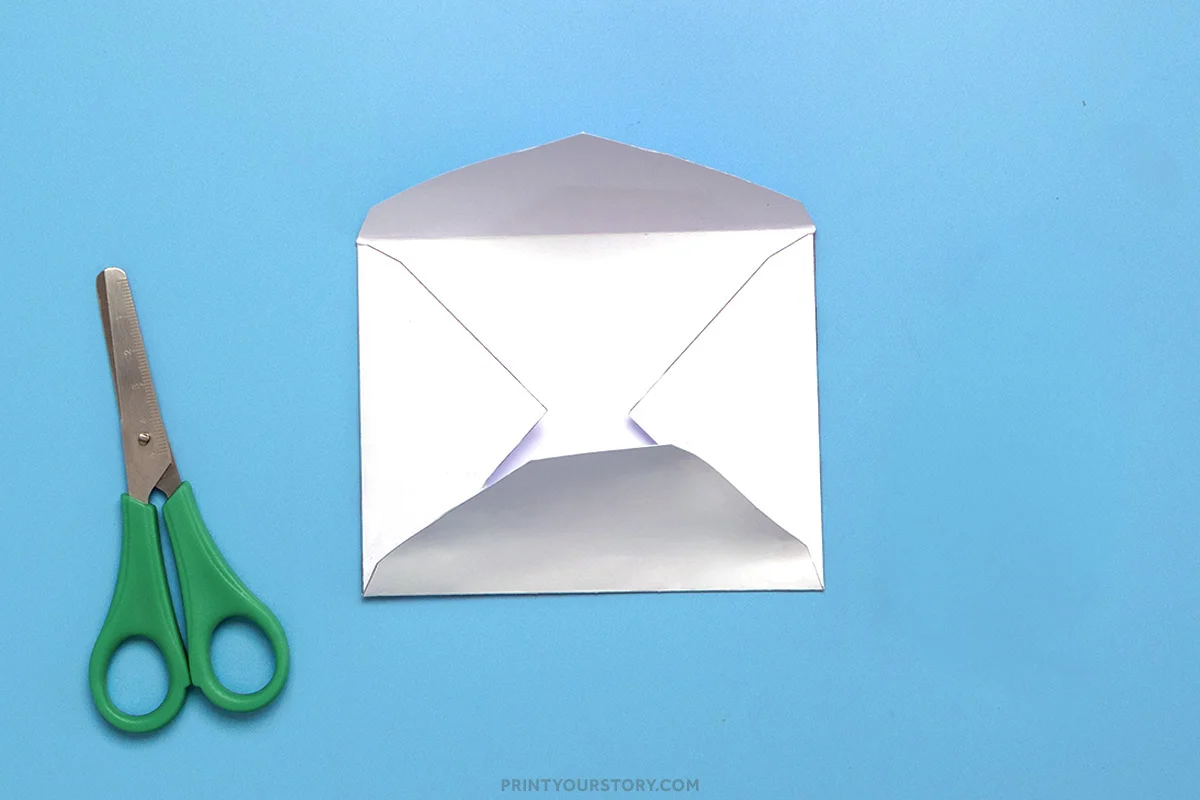 Folded white printable envelope with top flap open beside green-handled scissors on a blue background